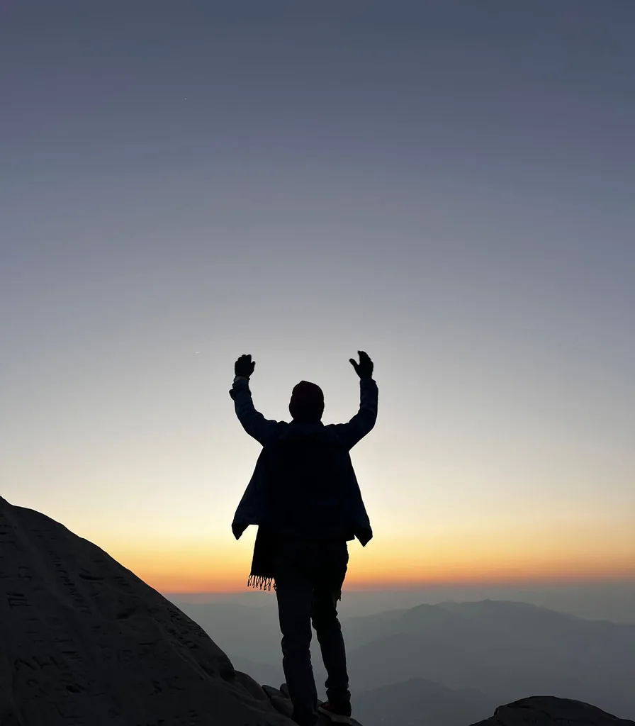 Person standing on a mountain ridge at sunrise, representing hope after trauma