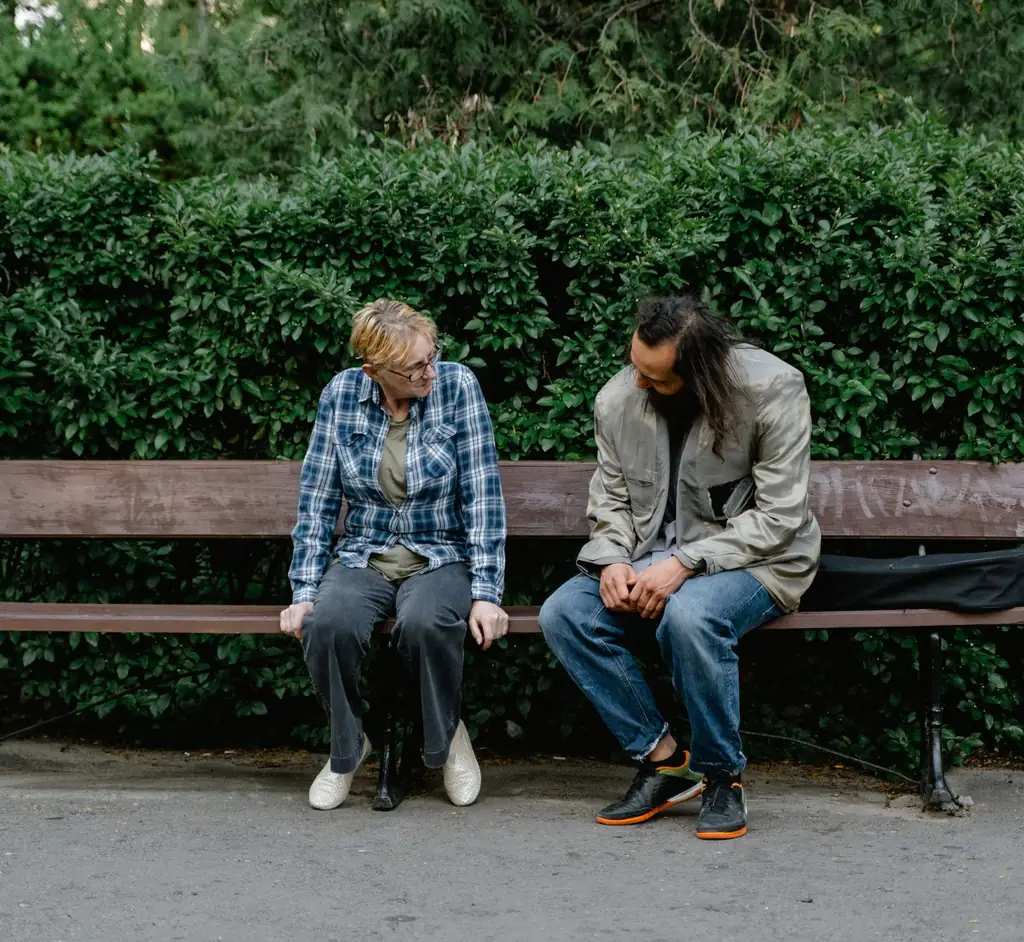 Two people talking on a park bench surrounded by greenery