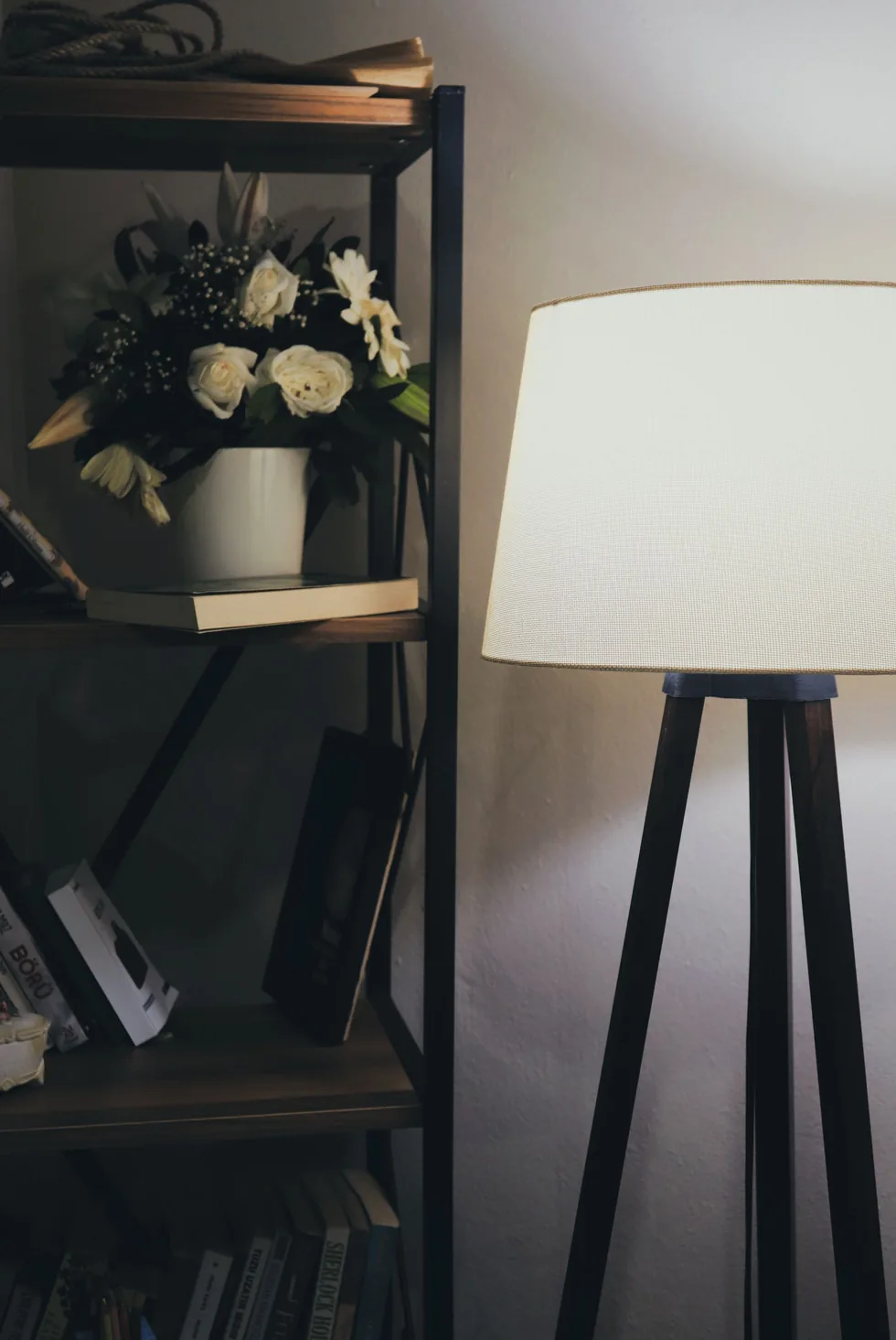 A warmly lit lamp beside a bookshelf with books and flowers