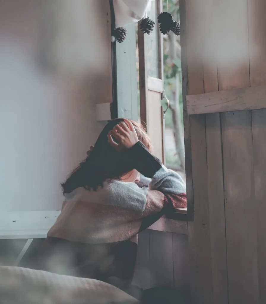 Woman sitting quietly by a window, reflecting while living with depression