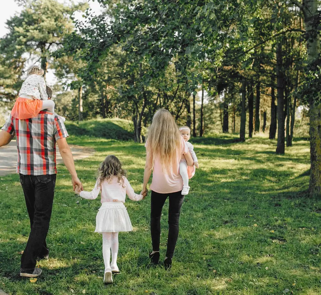 A family walking together under dappled sunlight in a green park
