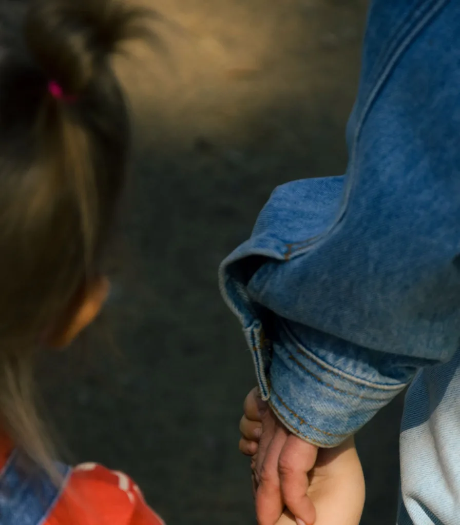 A child holding an adult's hand while walking along a sunlit path