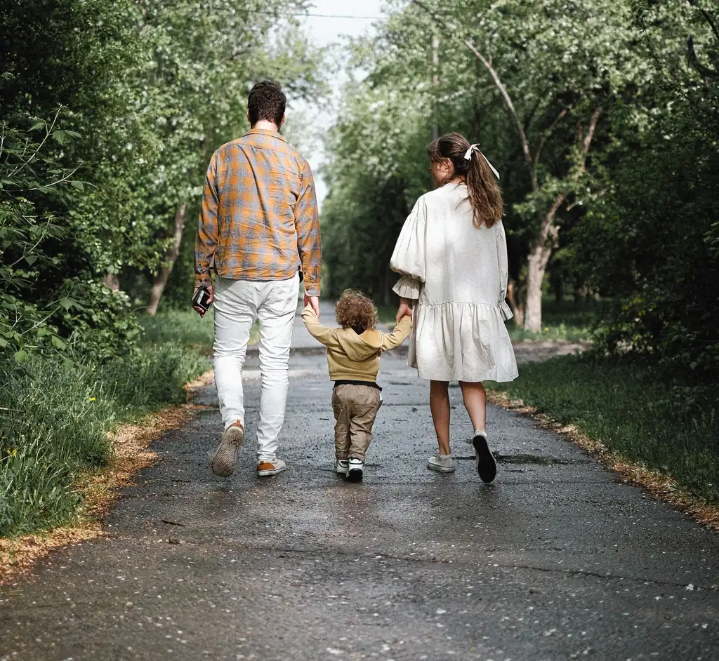 Parents and a small child walking a tree-lined path together