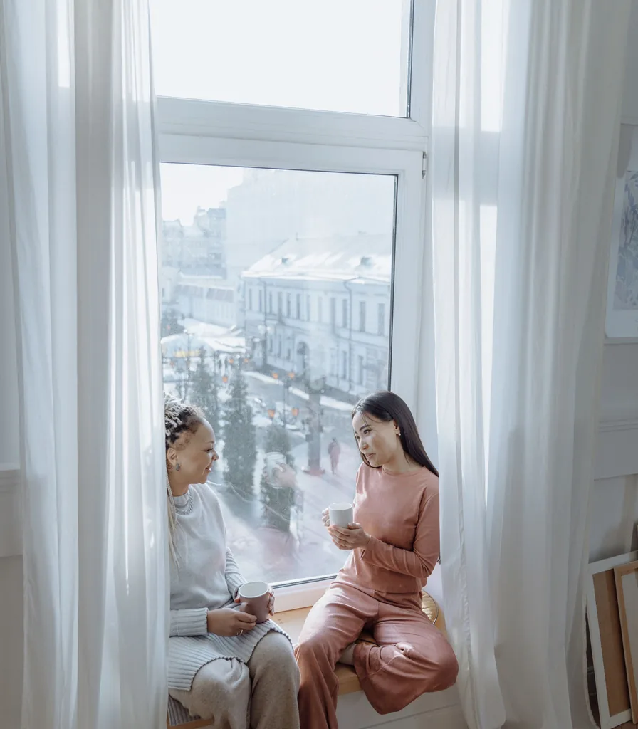 Two people talking openly over coffee beside a bright window