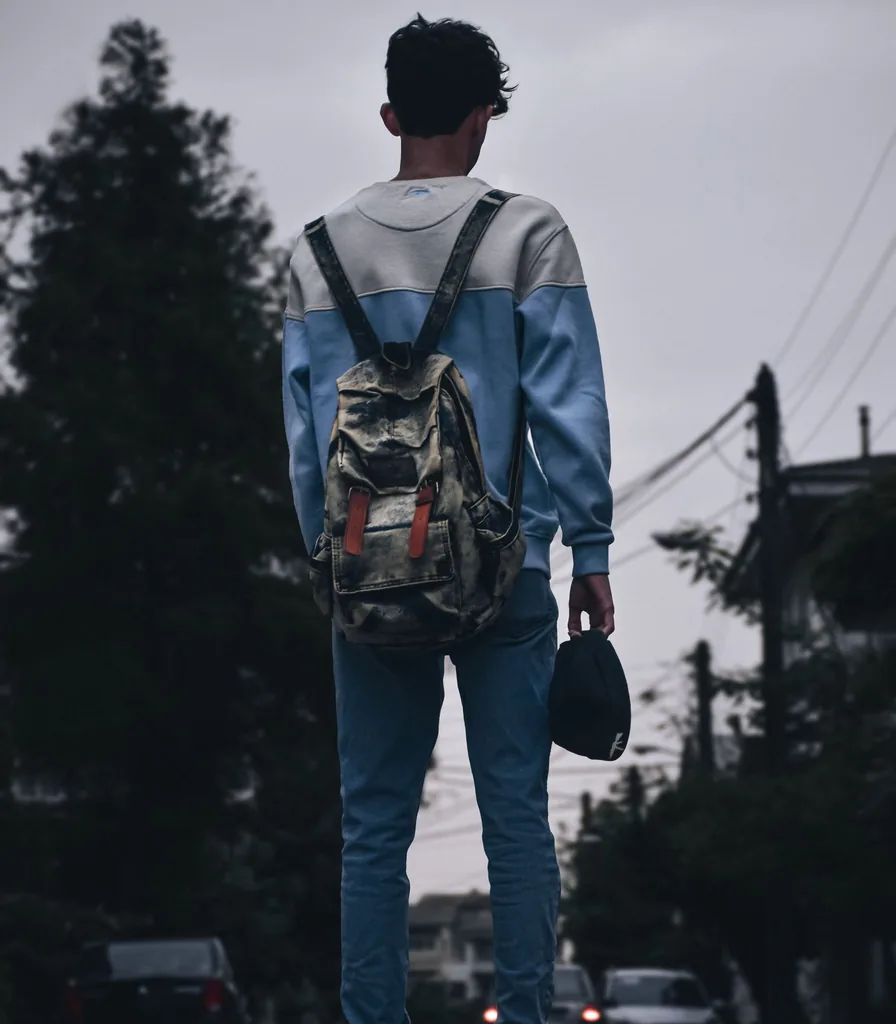 A young person with a backpack walking down a city street, seen from behind