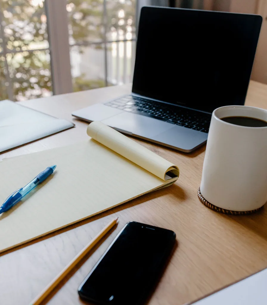 A laptop, coffee and notepad on a wooden desk in a quiet home workspace
