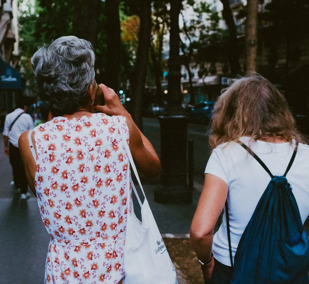 Two women walking along a tree-lined street, seen from behind