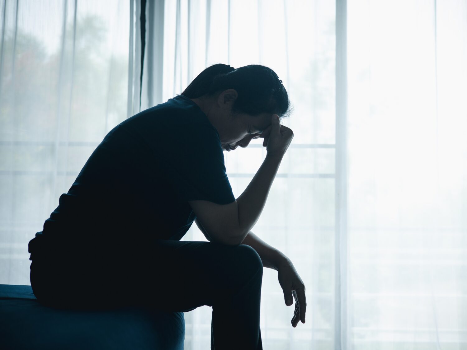 Silhouette of a parent sitting by a bright window with their head in their hand, looking exhausted