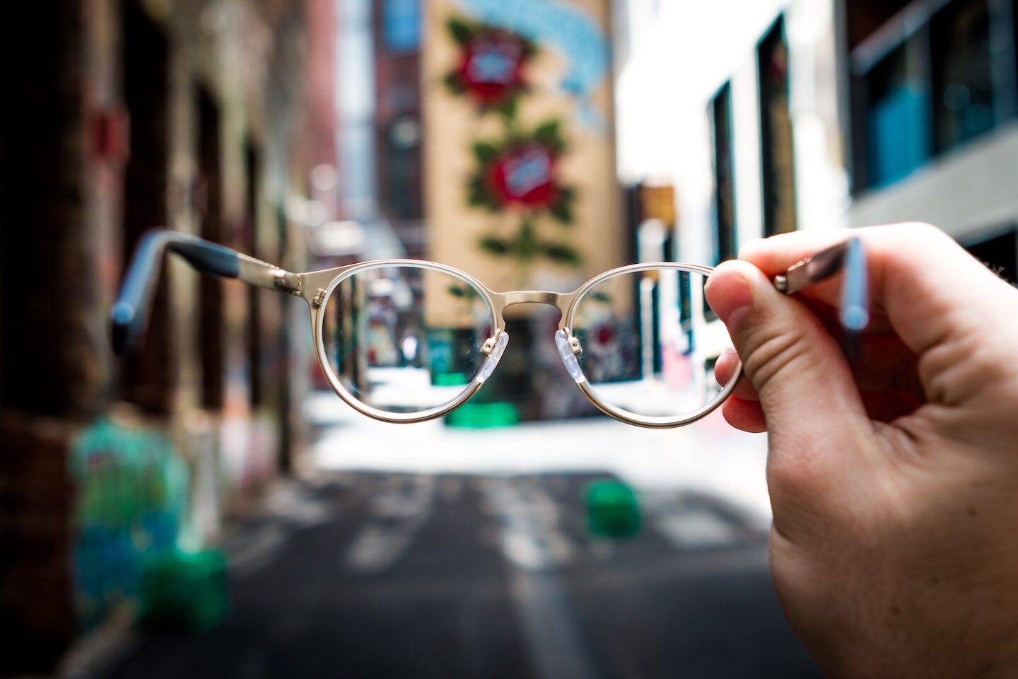 A hand holding up a pair of glasses that brings a blurry city street into focus
